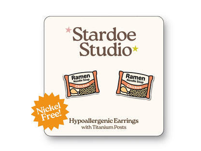 Cute instant ramen noodle stud earrings featuring a black bowl with yellow noodles and toppings playful food jewelry for kids and adults